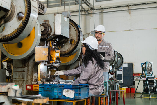 Engineer supervising female operator setting metal dies on mechanical power press ensuring precision and quality in a modern industrial manufacturing environment with heavy machinery