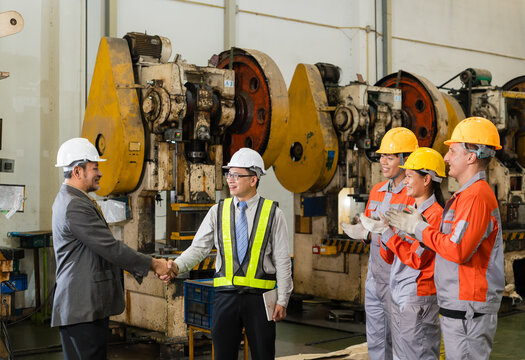 Senior manager in a suit shakes hands with an engineer in a hi-vis vest as three workers applaud near power presses