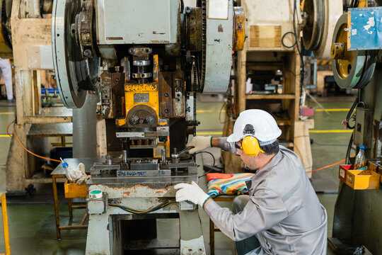 Male engineer adjusting mechanical power press with wrench in metal stamping factory highlighting skilled labor and industrial teamwork in the automotive parts manufacturing sector