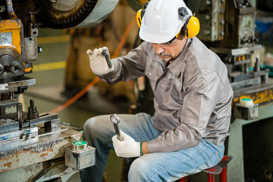 Machine operator examining threaded bolt and wrench beside a power press die ensuring precision and quality in a modern industrial manufacturing environment with heavy machinery