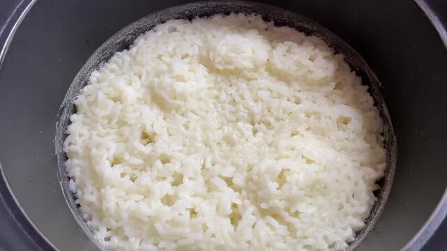 Close-up of freshly cooked white sticky rice inside a metal cooking pot, showing soft moist grains, a staple carbohydrate for Asian meals and domestic home cooking, simple nutritious food preparation.
