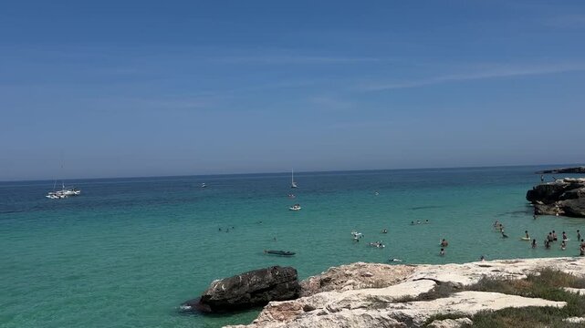 Swimmers enjoy crystal clear turquoise water in a rocky Adriatic cove near Monopoli in Apulia Italy. Scenic summer coastline with limestone cliffs, calm sea, leisure, tourism and beach recreation.