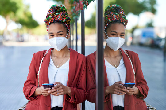 Woman wearing face mask standing in urban setting using smartphone