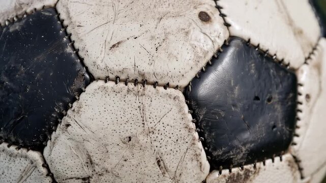 Tracking shot of worn leather soccer ball rotating slowly across neutral studio surface, revealing scuffed panels, stitched pentagons and aged texture