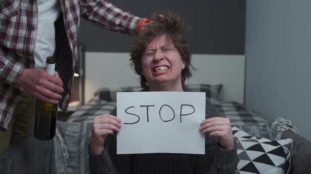 A distressed woman holds a "STOP" sign while an aggressive man with a bottle pulls her hair from behind. A powerful scene highlighting domestic violence, alcoholism, and the desperate cry for help