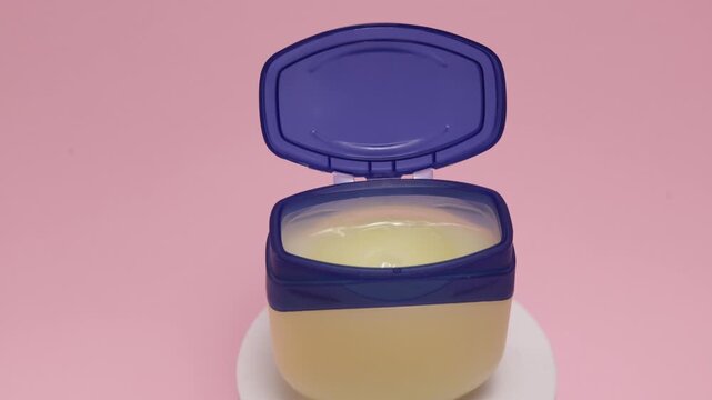 Petroleum jelly jar with open lid on a pink background
