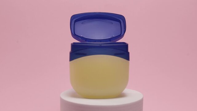 Petroleum jelly jar with blue lid open on a pink background