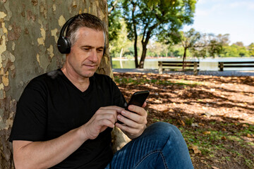 Fototapeta premium Active mature gentleman relaxing outdoors near a lake while using smartphone technology