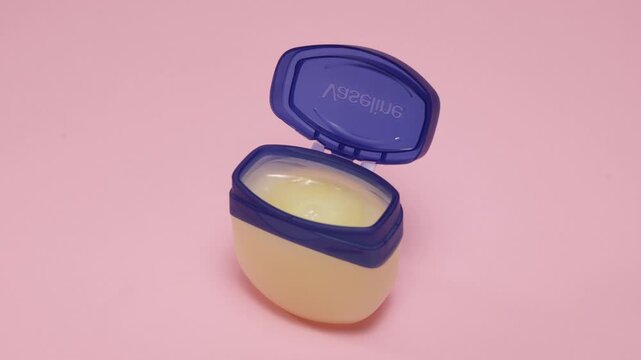 Petroleum jelly jar with blue lid open on a pink background