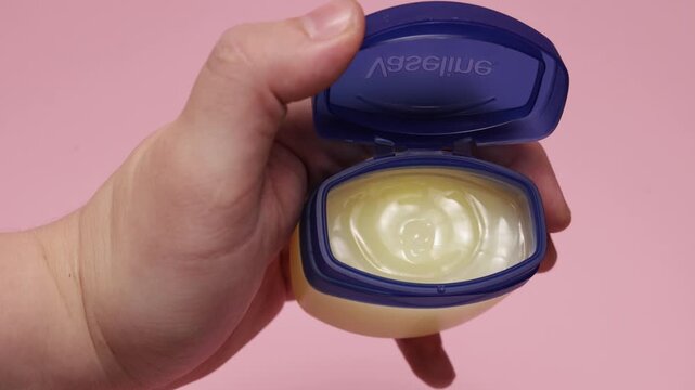 Hand opening a small jar of petroleum jelly for skin care