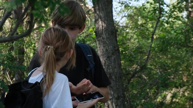 Close up of teenage brother and sister lost in a forest without adults arguing and checking a map on a smartphone. Children in danger. Hiking without adults is risky and dangerous.