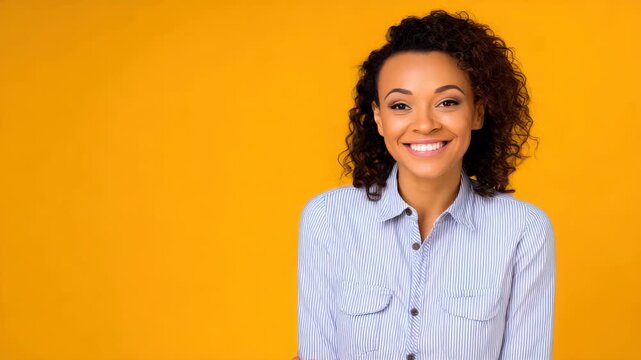 Happy young woman with curly hair smiling and posing on vibrant yellow background, portrait of a cheerful female in a striped shirt, studio shot