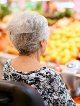 Elderly woman mobility scooter grocery shopping fruit display supermarket aisle rear view senior consumer retail store fresh produce colorful background