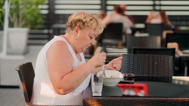 Profile of mature overweight woman eating healthy salad at outdoor cafe.