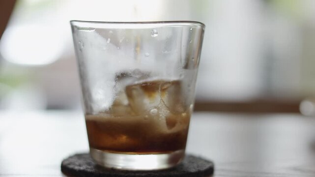 Close up of pouring dark carbonated soda into a glass filled with ice cubes. Refreshing cold beverage with fizz and bubbles. Summer thirst quenching and cooling drink concept.