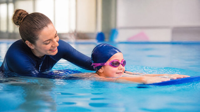 Professional Swimming Instructor Teaching a Young Girl to Swim in an Indoor Pool with a Kickboard, Illustrating Childhood Development, Safety, Education, and Encouraging Fitness for Kids
