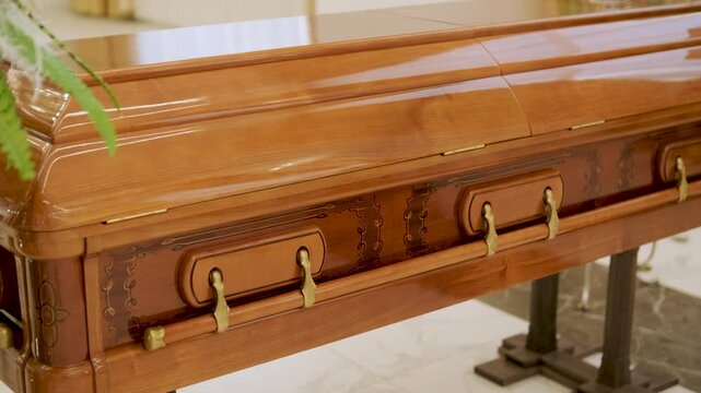 Closed wooden coffin in a bright funeral home or chapel. Solemn farewell ceremony setup with white floral arrangements, empty chairs, and a religious icon.