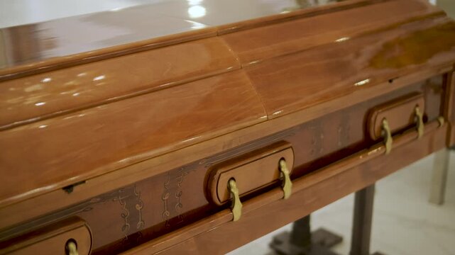 Closed wooden coffin in a bright funeral home or chapel. Solemn farewell ceremony setup with white floral arrangements, empty chairs, and a religious icon.
