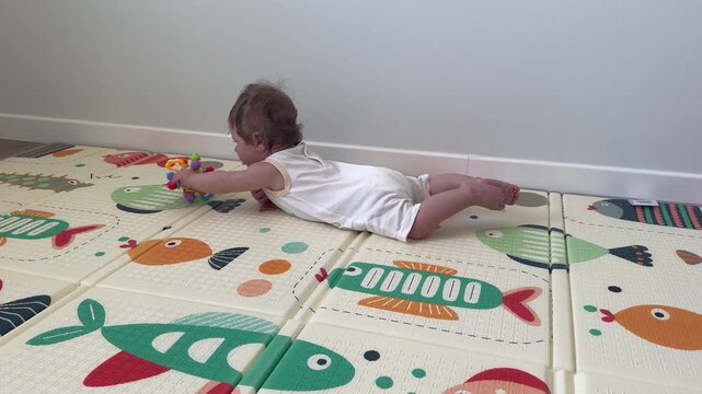 Infant lies on stomach playing with plastic rattle toy on colorful soft play mat indoors. Early child development focus highlights motor skills growth sensory discovery and playful learning at home.