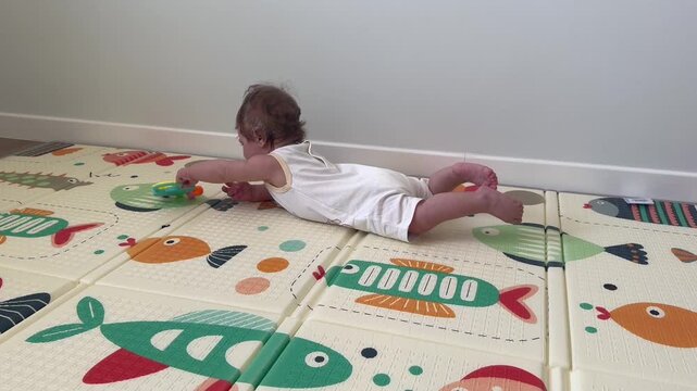 Infant lies on stomach playing with plastic rattle toy on colorful soft play mat indoors. Early child development focus highlights motor skills growth sensory discovery and playful learning at home.