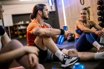 Fototapeta premium Athletic group resting and drinking from shaker bottles in the gym