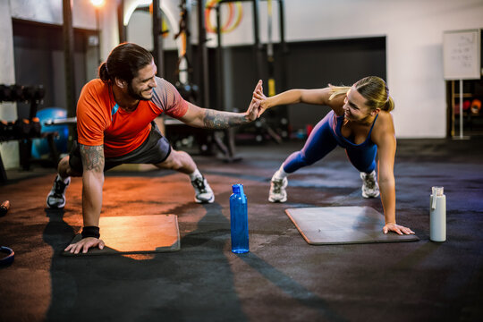 Man and woman doing plank and giving high five in the gym