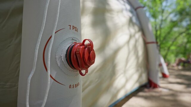 A close-up view of a red air valve on an inflatable camping tent showing the 7 PSI and 0.5 BAR pressure markings. Concept of camping equipment, outdoor technology, and efficient setup.