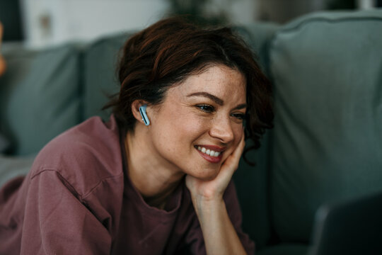 Woman smiling using laptop and earbuds at home