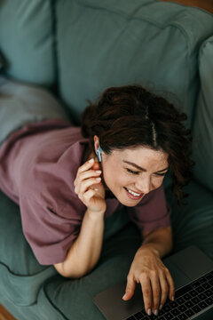 Woman relaxing on couch using laptop and earbuds