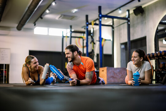Athletic friends toasting with shaker bottles and smiling on the gym floor