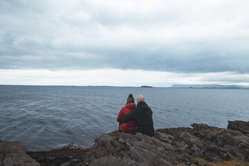 Fototapeta premium Couple sitting together on a rocky Icelandic coast and looking across the cold ocean