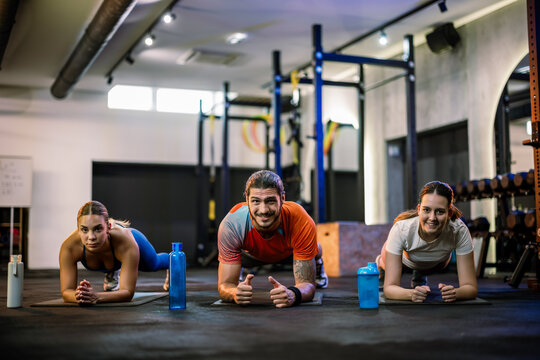 Three athletic friends doing plank exercise with shaker bottles on the gym floor