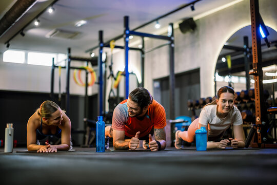 Three athletic friends doing plank exercise together on the gym floor