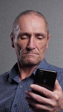 Worried mature man holding a mobile phone, his face showing deep concern and distress as he scrolls through the screen, reacting to receiving bad news, feeling anxiety and sadness