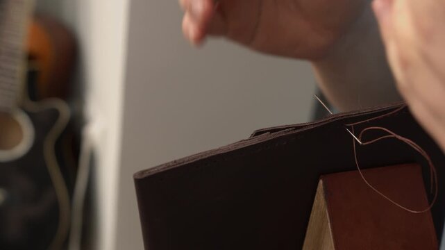 Craftsman hand stitching a brown leather wallet using a saddle stitch technique in a workshop