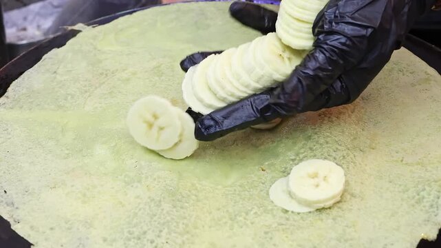Cook slicing mango for tropical fruit crepe filling. Close-up of fresh fruit preparation with mango and banana. Concept of street dessert, healthy food, cooking process and tropical ingredients