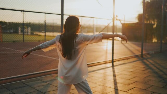 Back view of mature woman swinging arms on a bright outdoor court.