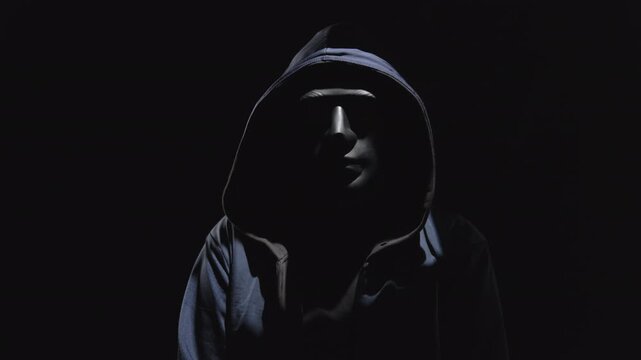 Man hiding face behind black mask and hood on head gives interview