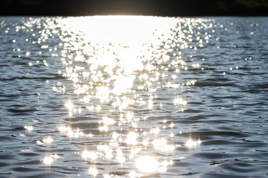 Blazing light floods the lake horizon and scatters into sparkling points across dark rippled water A vivid summer scene filled with motion and reflective beauty perfect for backgrounds