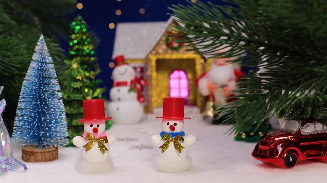 Two snowmen in red hats against the backdrop of a Christmas house with a snowman and Santa Claus