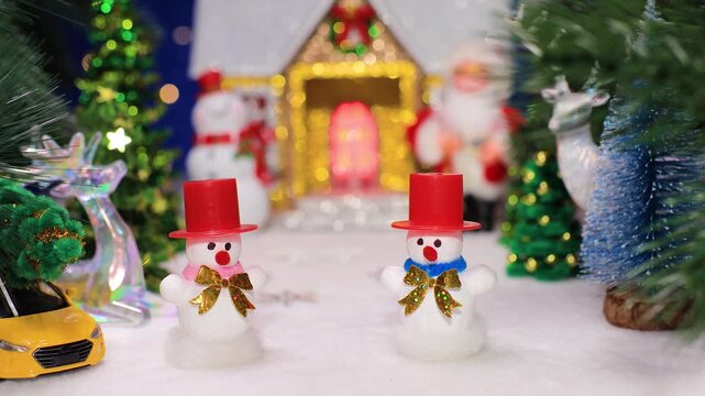 Two snowmen in red hats with a yellow car against the background of a Christmas house with a snowman and Santa Claus