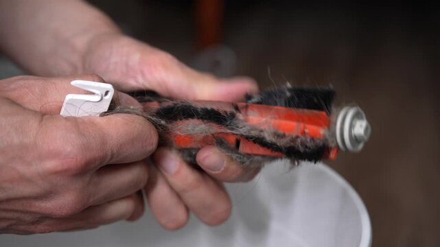 Process of maintenance of household appliance, male hands using cutting tool to remove accumulated dust, long hair, animal fur from very dirty vacuum cleaner roller brush. Shooting in slow motion.