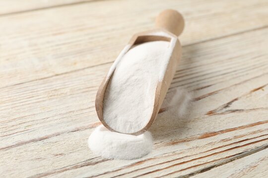 Baking soda in scoop on color wooden table, closeup
