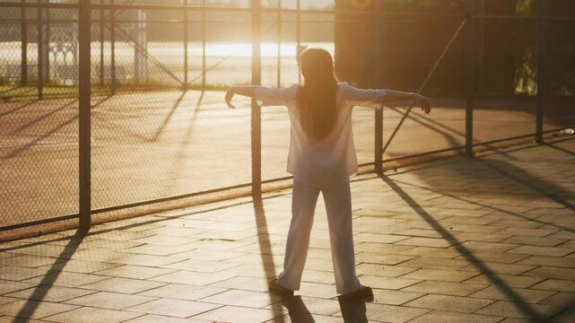 Mature female performing mindful tai chi on outdoor court during warm sunrise.