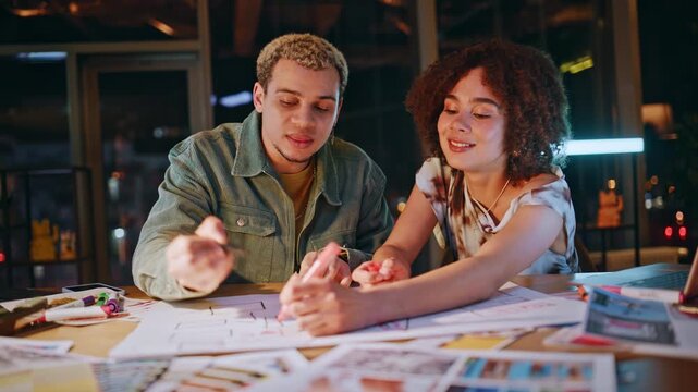 Two young designers sketching floor plan discussing project office at night