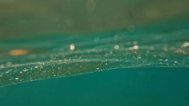 Fotograf&iacute;a art&iacute;stica de la superficie del agua vista desde dentro, con burbujas y reflejos abstractos.