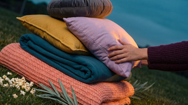 Stacked colorful blankets and pillows on grass during evening 