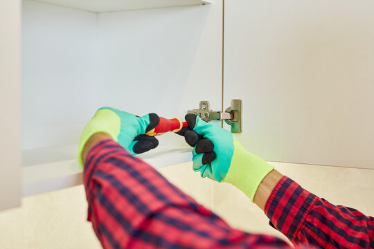 Professional furniture worker assembling kitchen closets and cabinets. Repairman Repairing Cabinet Hinge In Kitchen. Helping People in New House. Male hand adjusting a mechanism.
