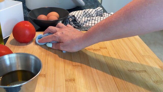 Female hand using a blue microfiber cloth to wipe and disinfect a wooden surface. 