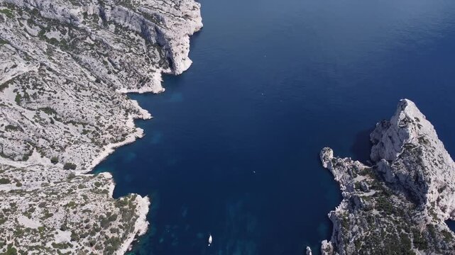 Cinematic aerial drone shot of the stunning white limestone cliffs of the Calanques dropping into deep dark blue Mediterranean water, beautiful coastal landscape in France